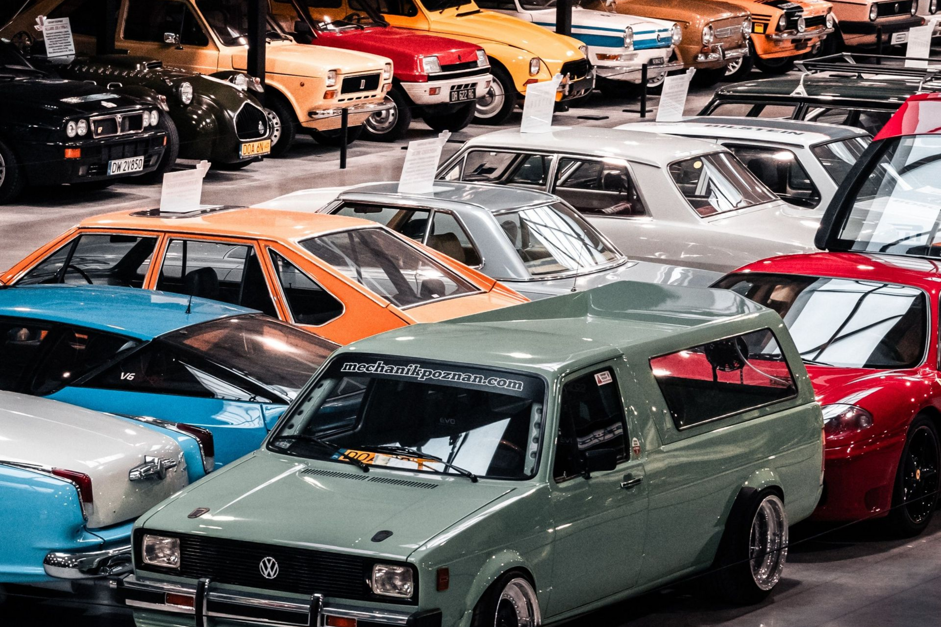 Classic cars displayed in a garage showroom, including green, red, and white vintage vehicles.