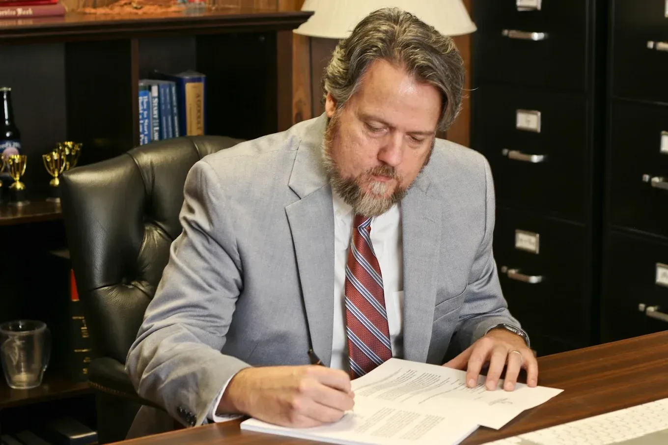 Man in a gray suit signing papers at a desk in an office