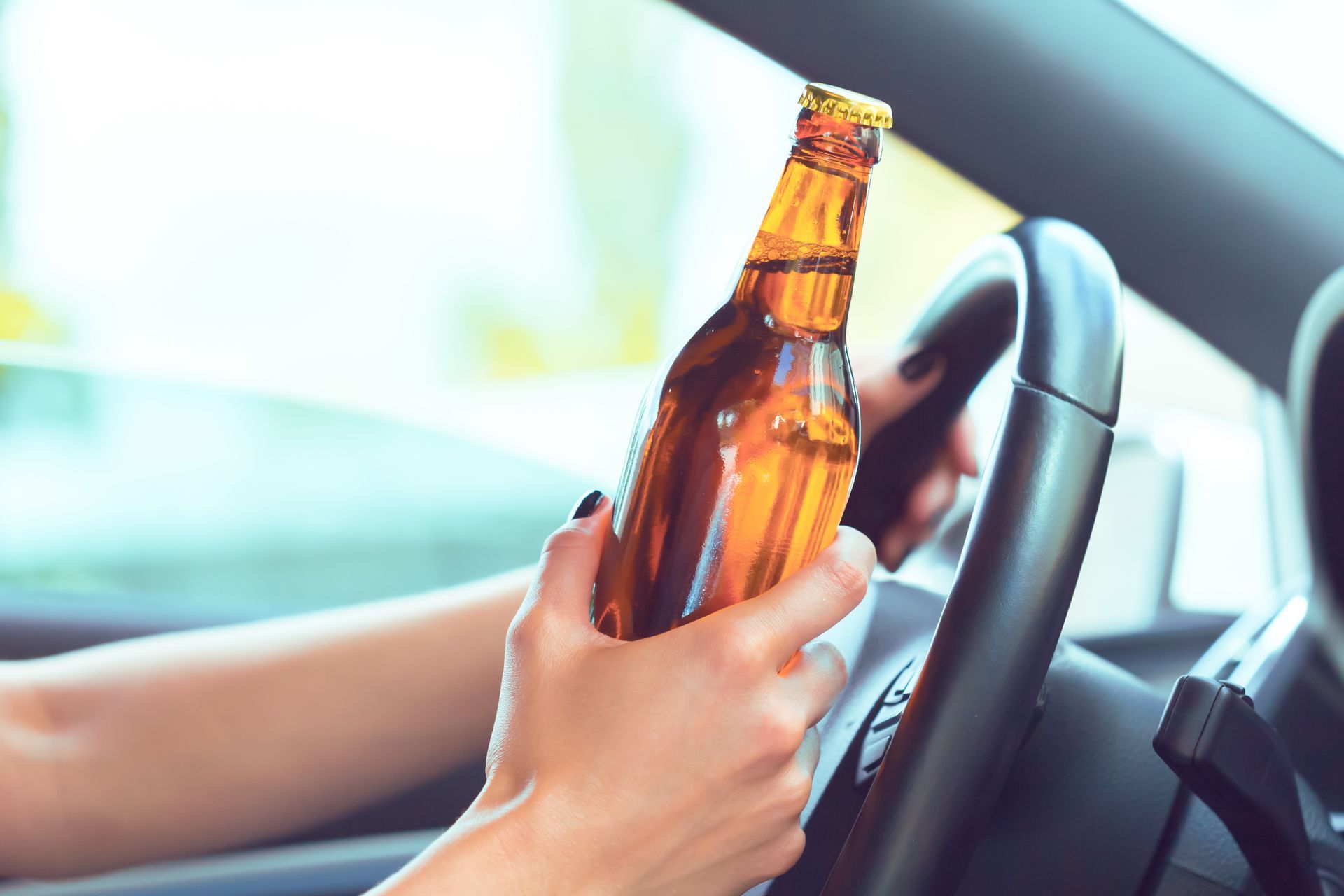 Hands holding an amber bottle in a car, near the steering wheel.