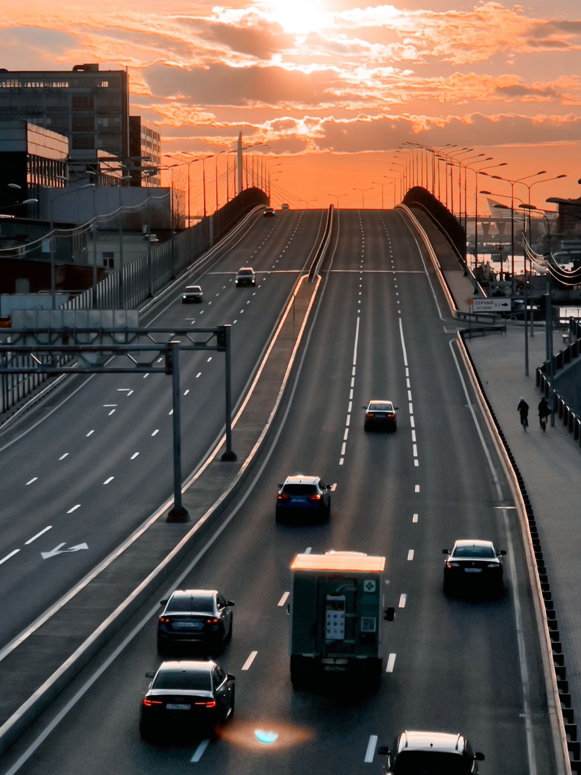 Sunset over a city highway with several cars driving toward the horizon