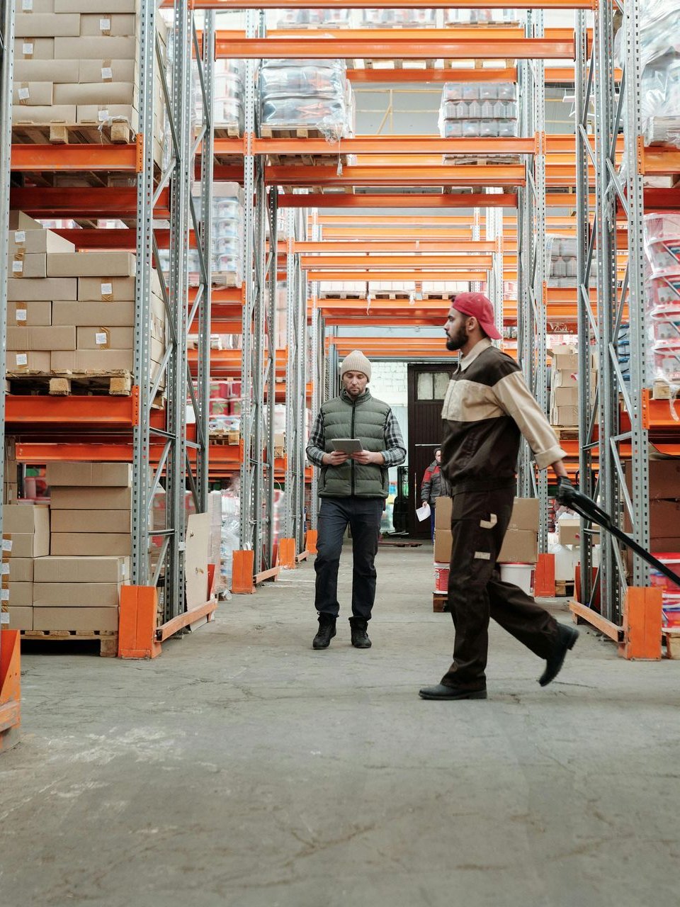 Two workers walking through a warehouse aisle with tall orange storage racks