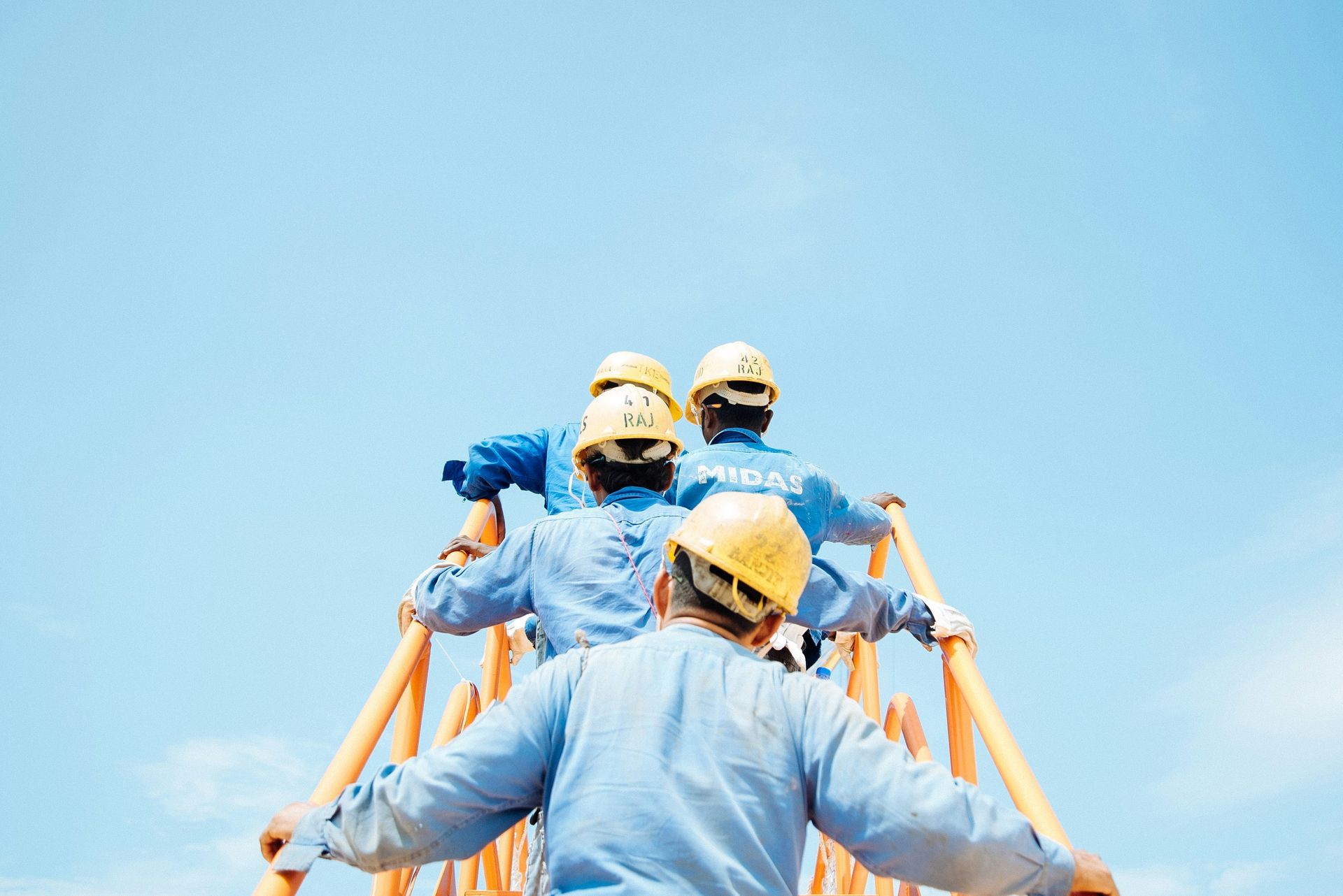 Workers in blue uniforms and helmets standing together against a bright blue sky