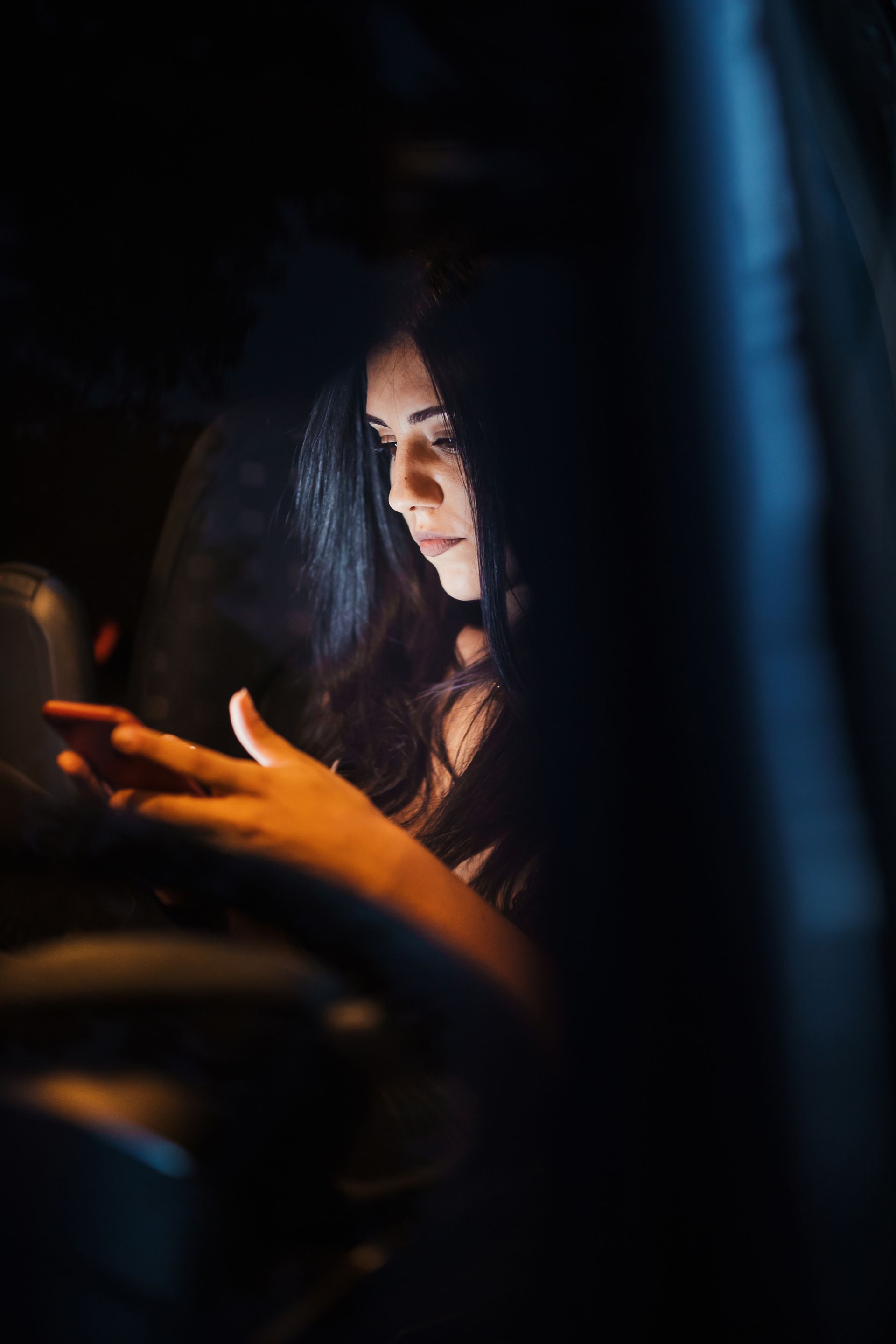 Woman lit by a warm phone glow in a dark setting, looking down at her screen