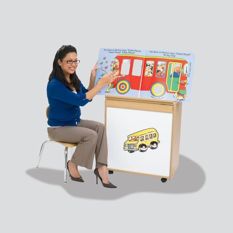 A woman is sitting on a chair reading a book about a school bus