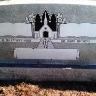 Engraved grey stone headstone featuring a church, flowers, and the text