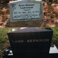 Two headstones in a grassy area: one gray with nature carvings, the other black with 