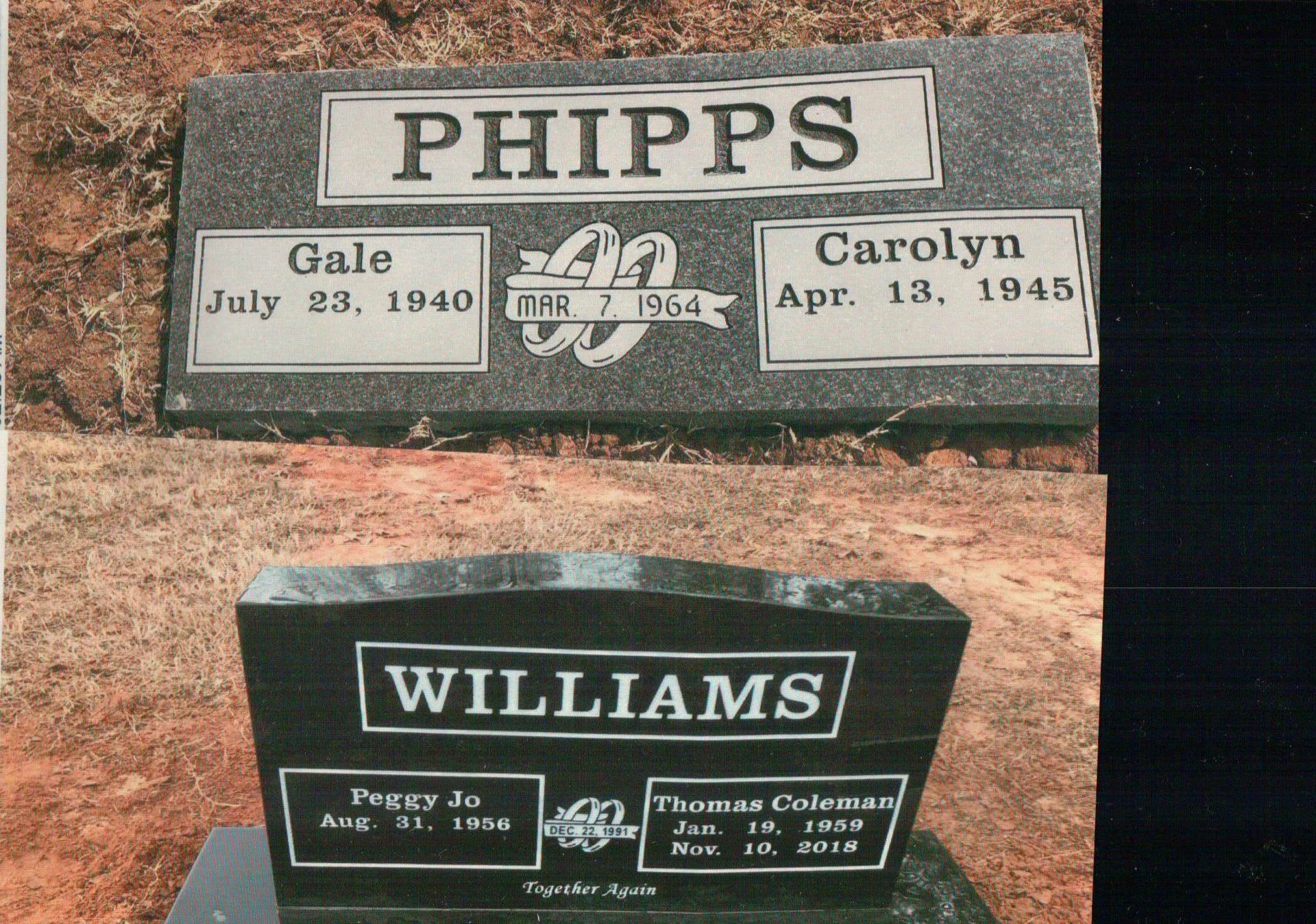 Two black granite grave markers on red dirt; one labeled 