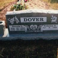 A granite grave marker for Dennis L. and Rebecca A. Dover with floral decorations on a cemetery plot.