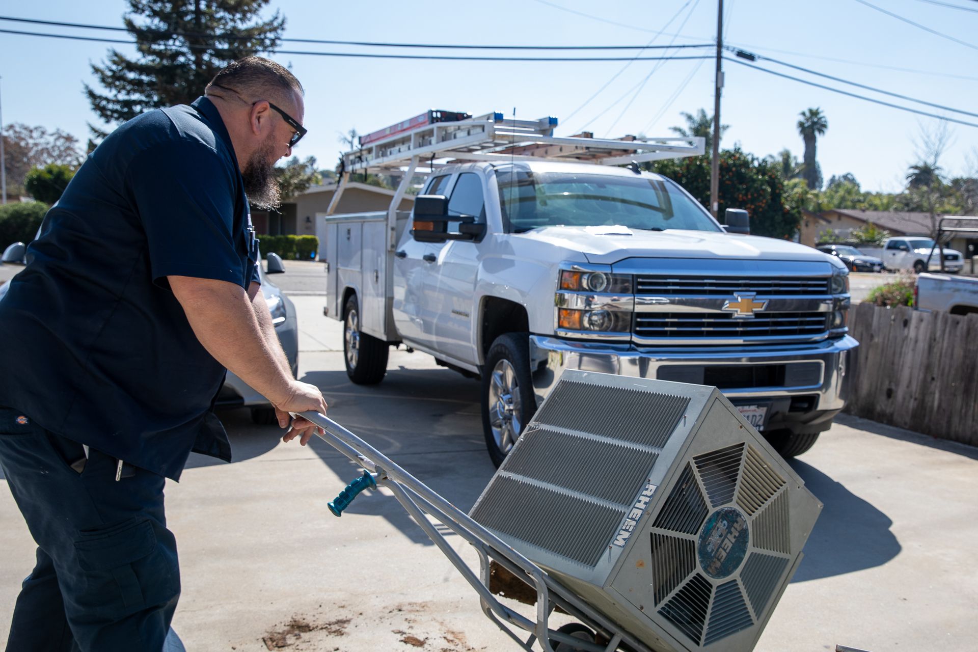 A man is pushing an air conditioner on a dolly in front of a truck