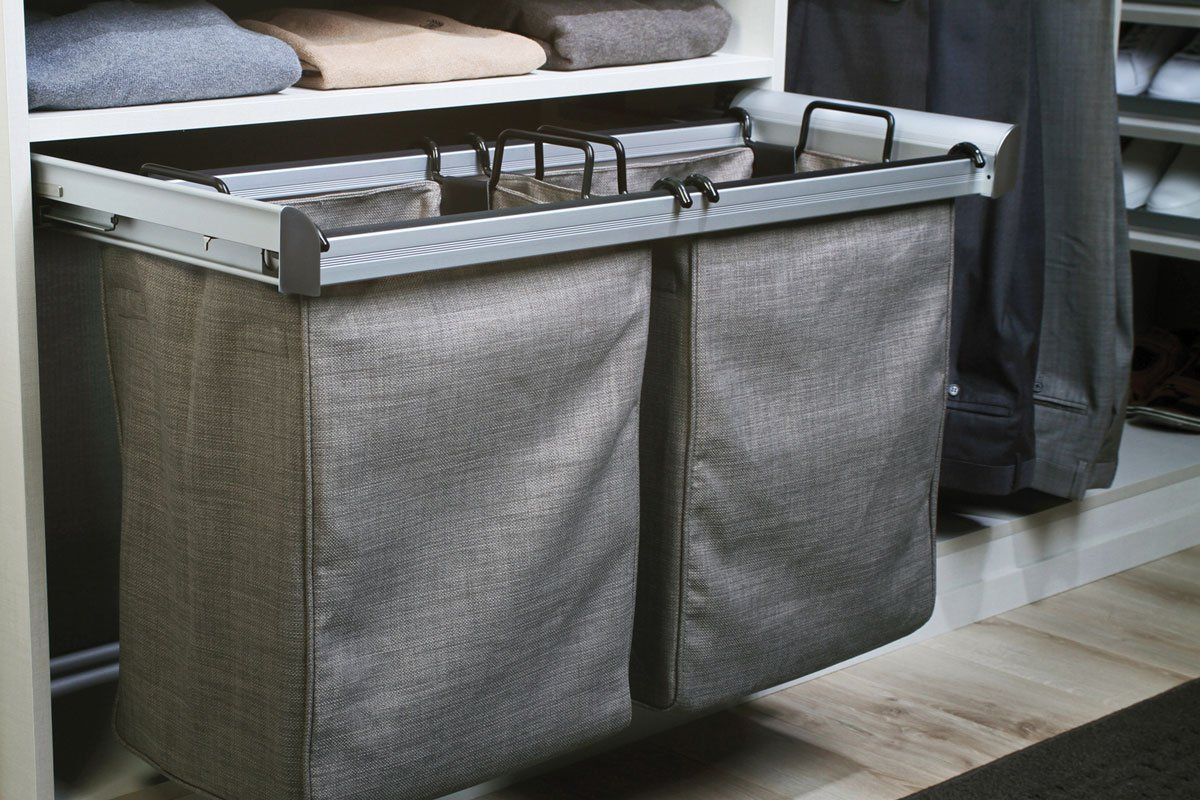 A laundry basket is pulled out of a closet filled with clothes.