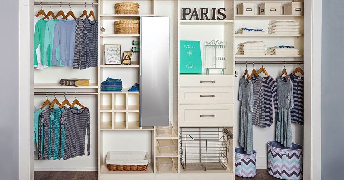 Organized walk-in closet with hanging clothes, shelves, drawers, shoes, and storage bins in white and wood tones