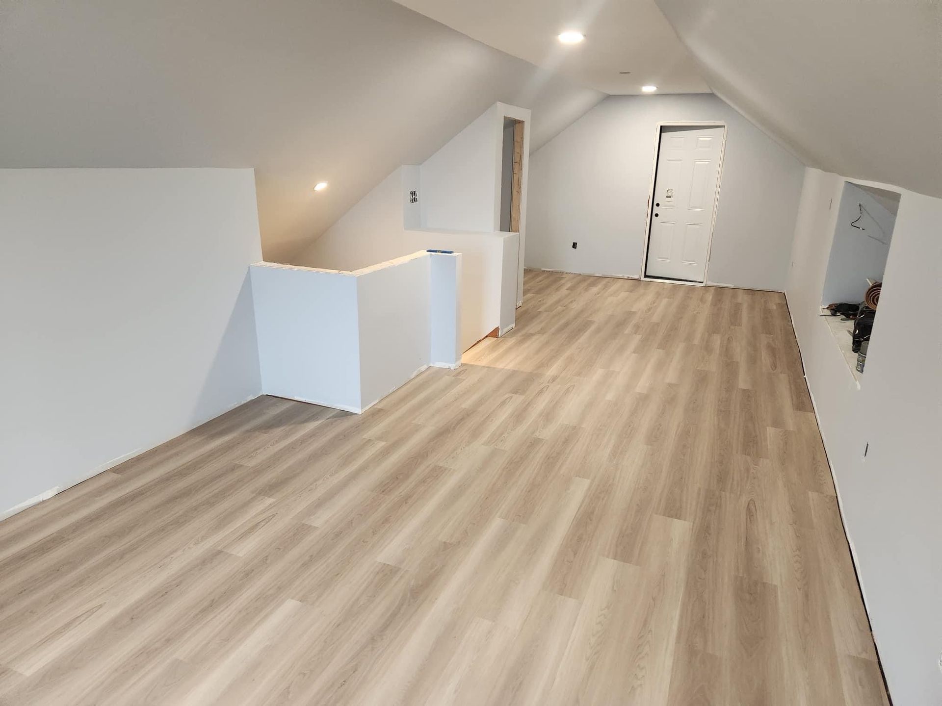 An empty attic with hardwood floors and white walls.