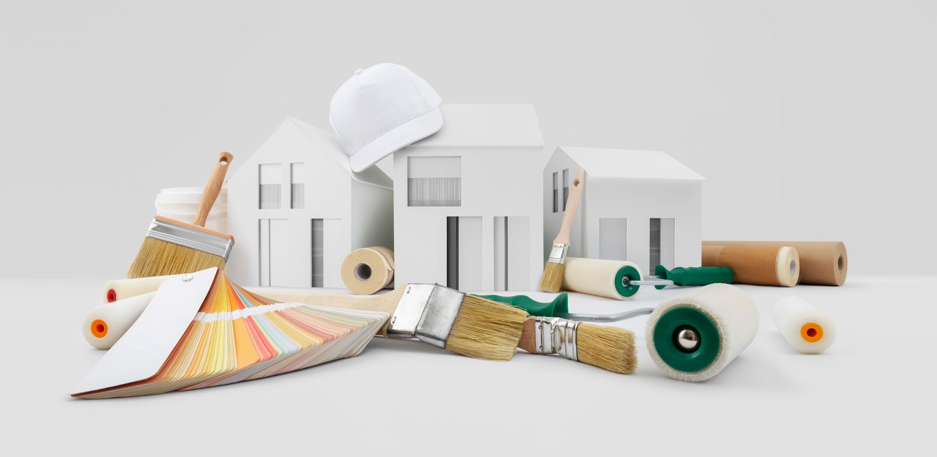 There is a model of a house surrounded by paint rollers and brushes.