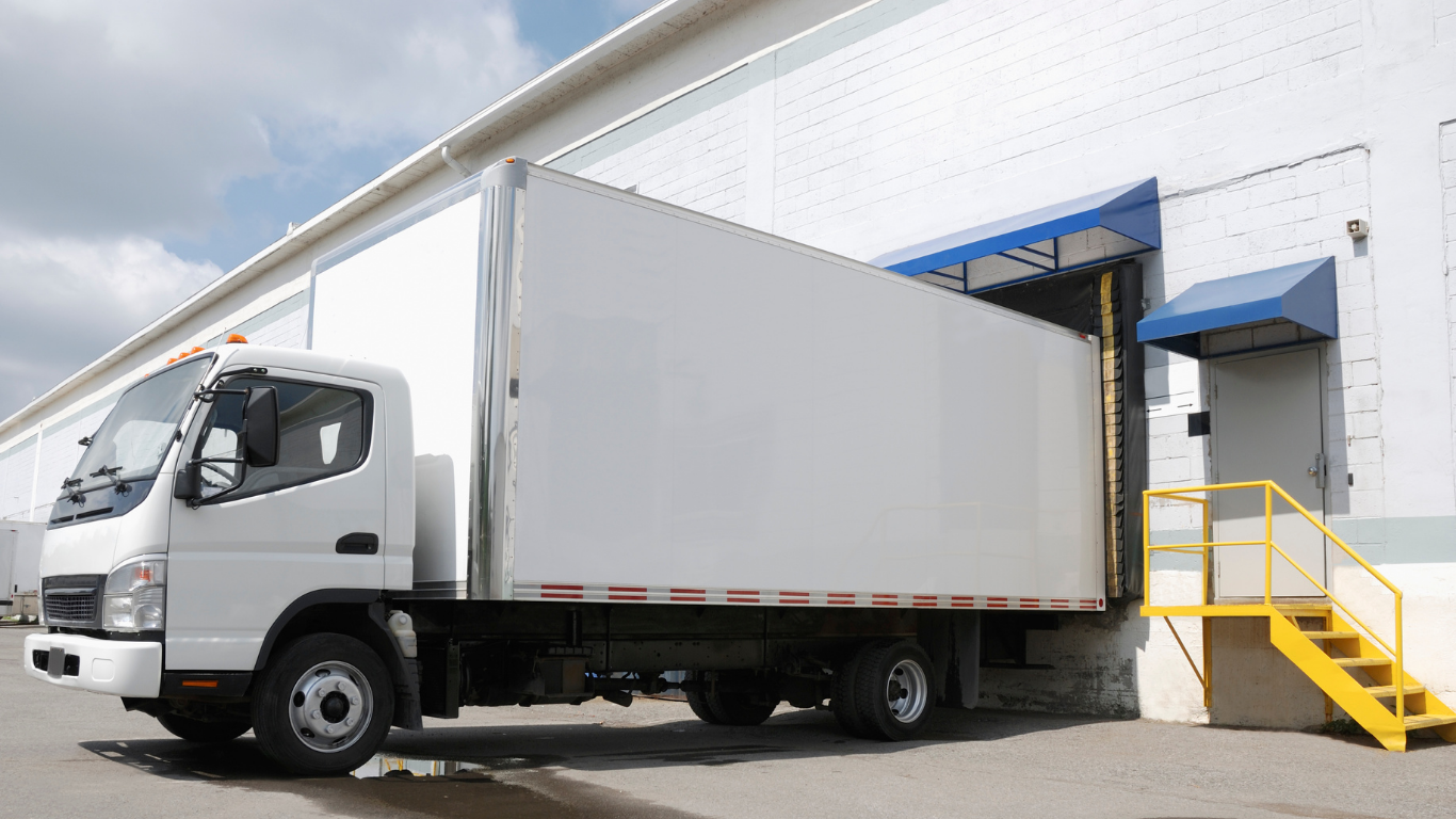 White truck backing up to a warehouse loading dock, steps on right.