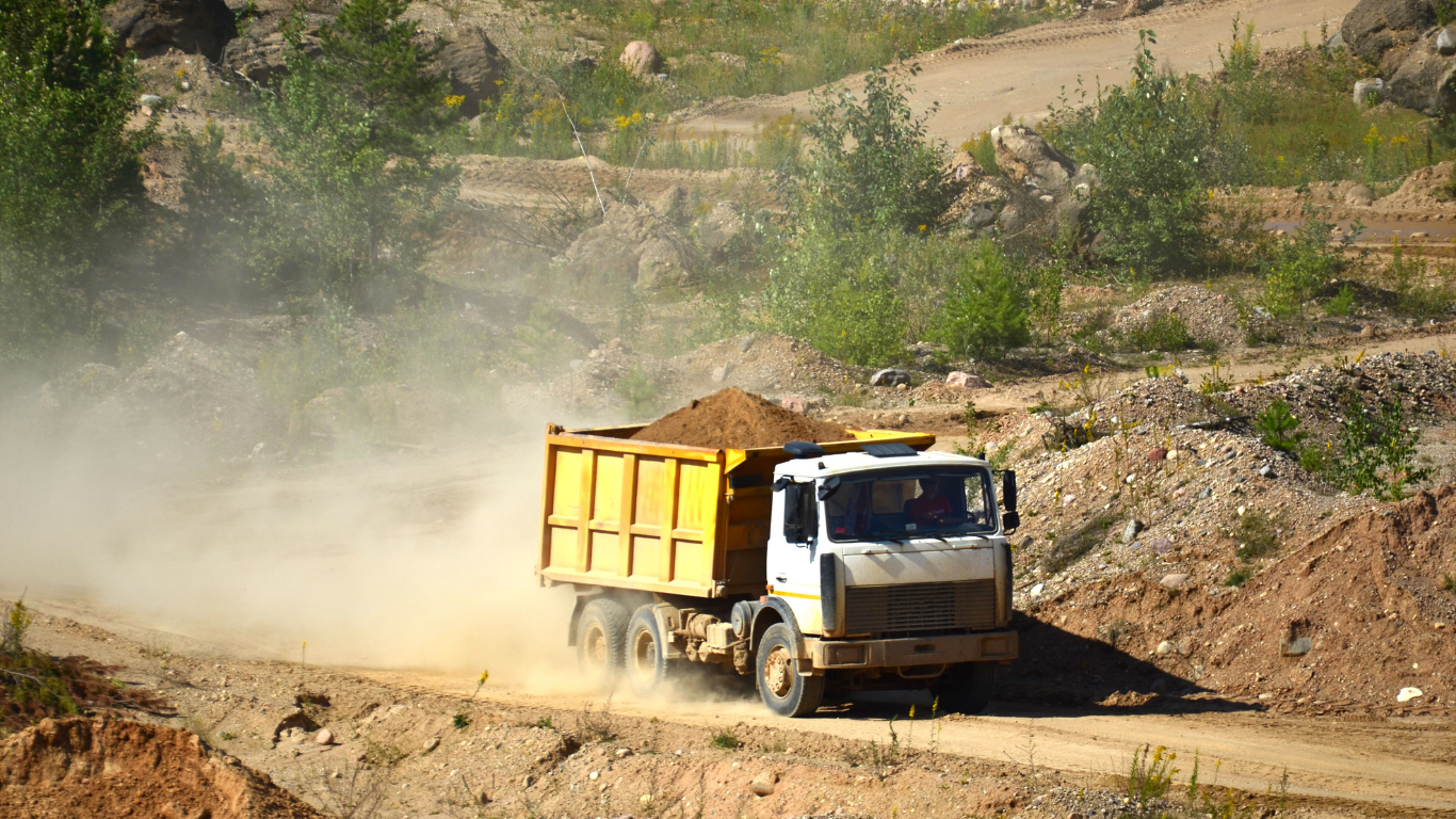 Dump truck driving on a dusty road in a quarry, carrying a load of sand.