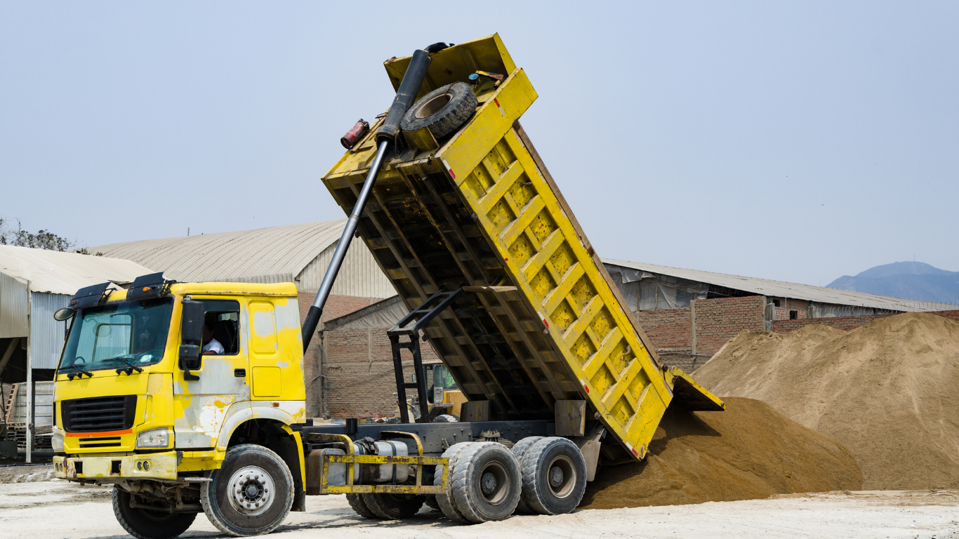 Yellow dump truck unloading sand.