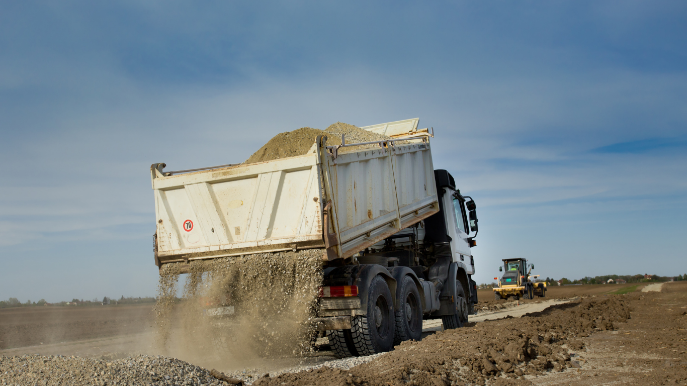 Dump truck unloading gravel on a construction site; blue sky.