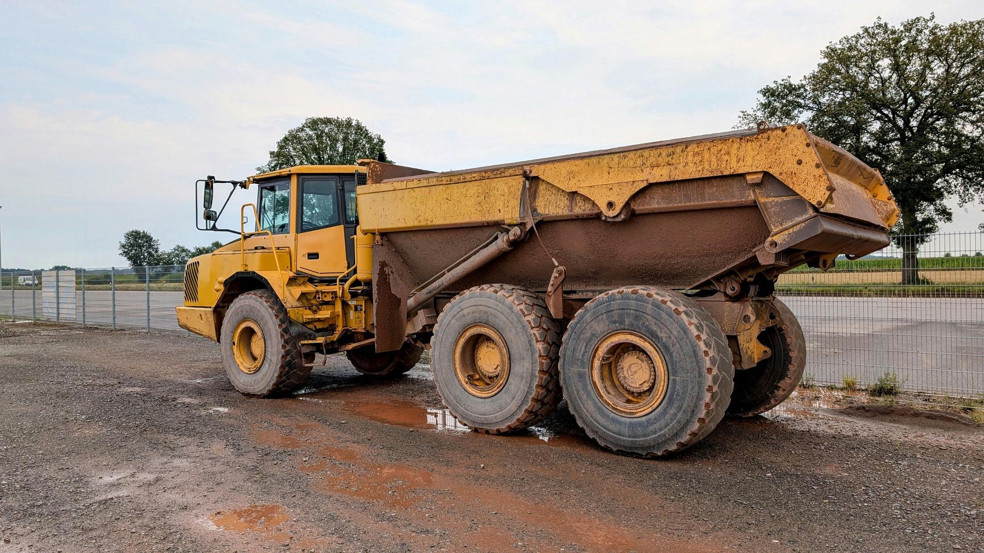 Yellow articulated dump truck covered in mud on a muddy road.