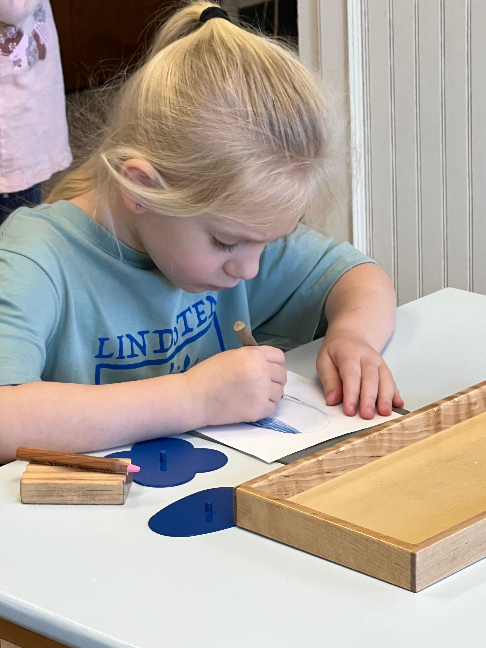 Child concentrating on the metal insets in a Montessori primary classroom