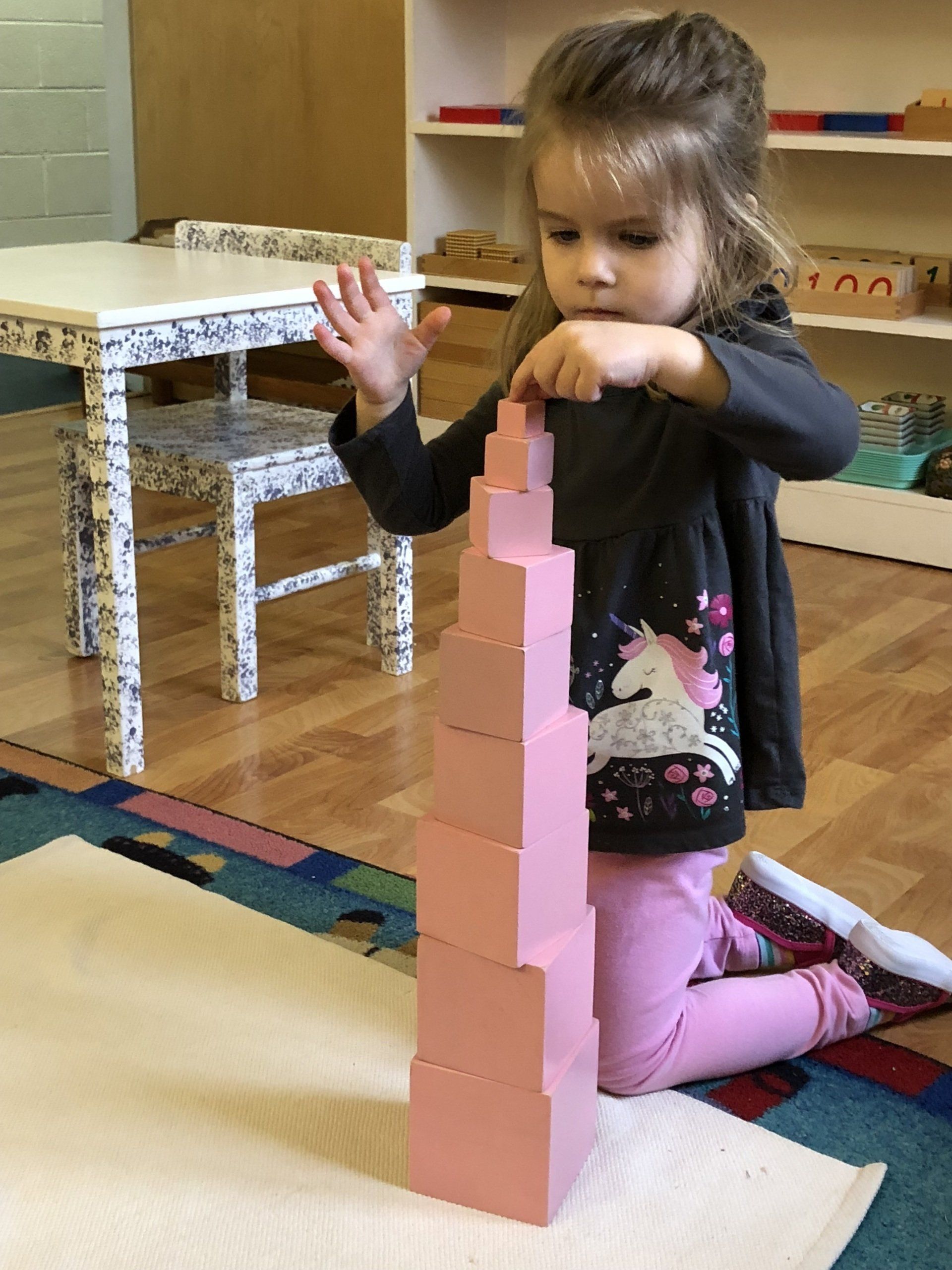 Montessori Child building a tall tower with pink wooden blocks indoors.