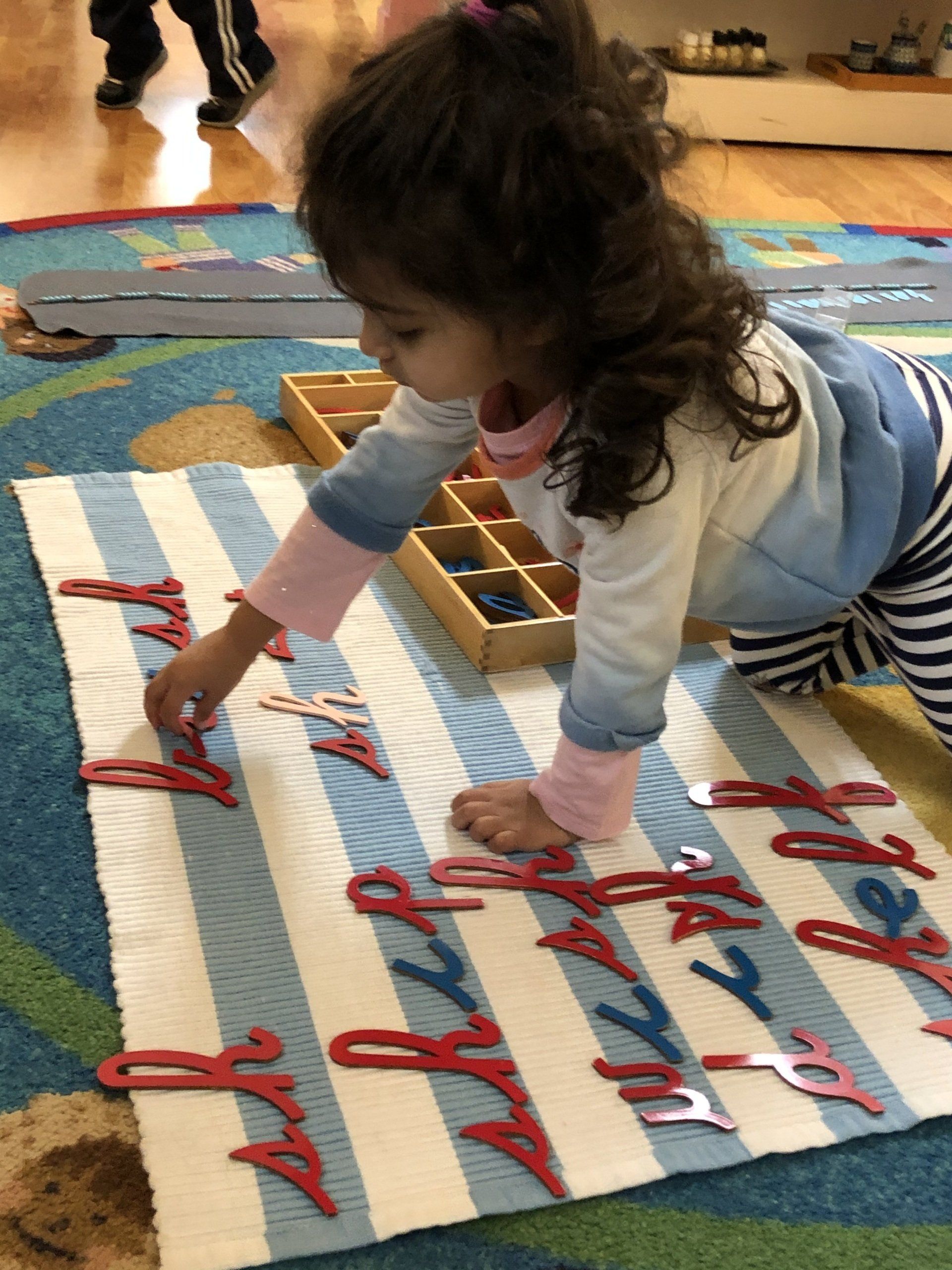 Montessori  child playing with wooden letter pieces on striped mat.