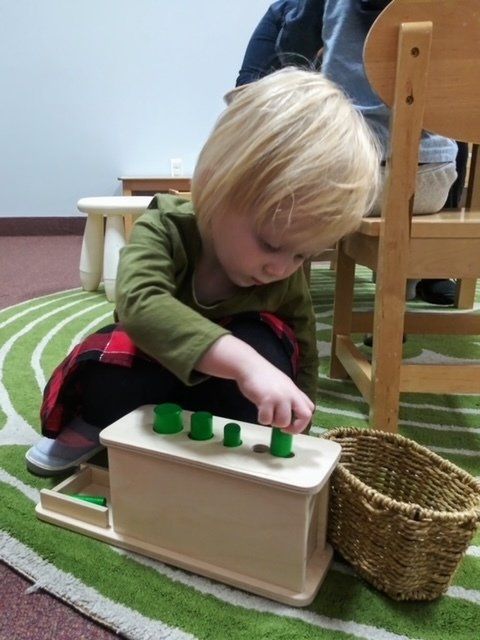 Montessori Child playing with wooden cylinder block toy on green rug.