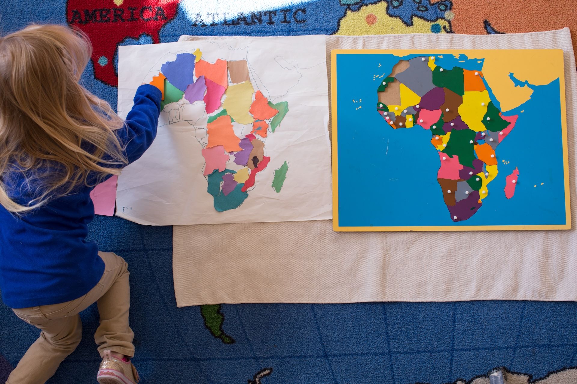 Child placing colorful map pieces on an Africa map display in a classroom