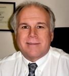 A man in a white shirt and tie is smiling for the camera.