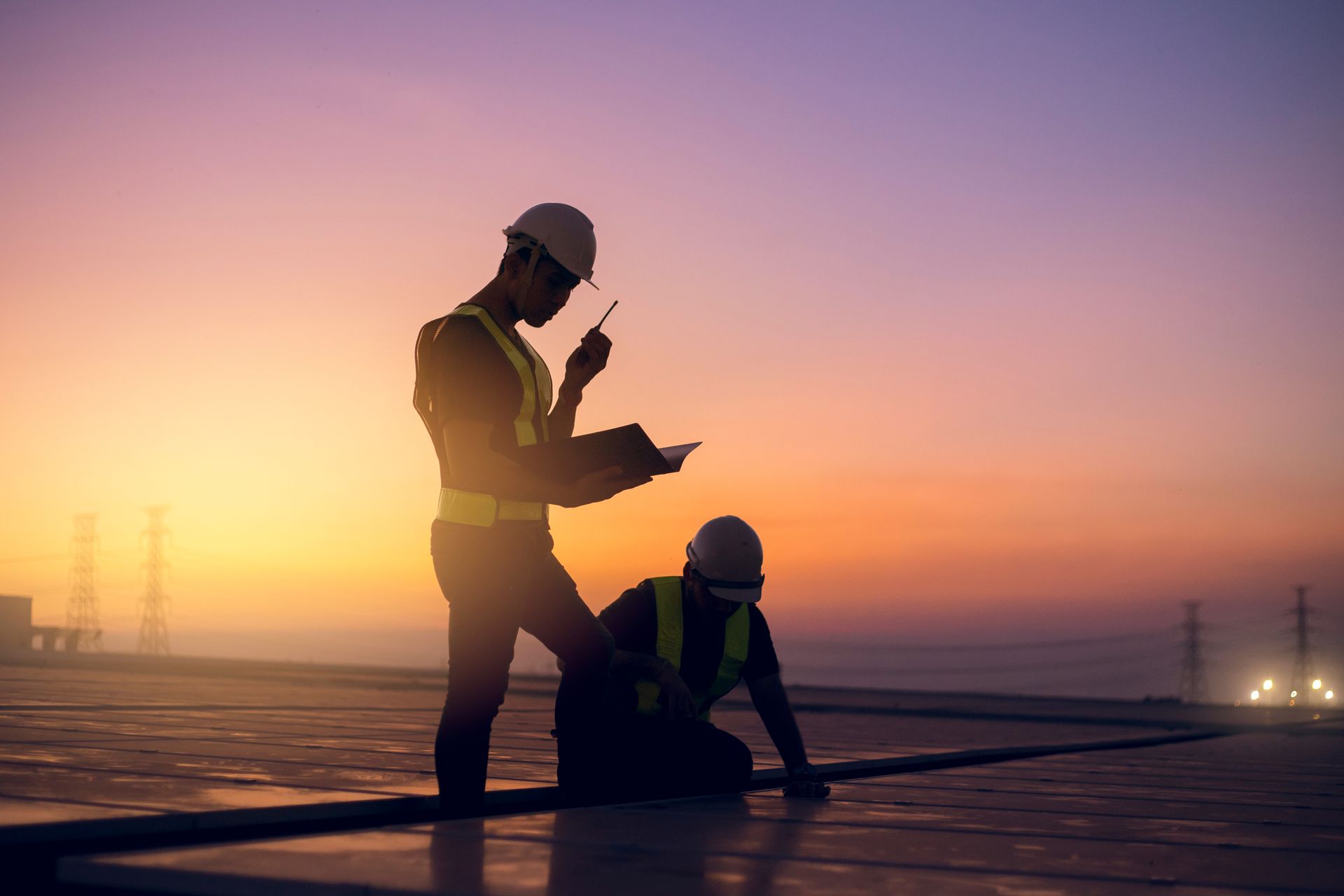 Two construction workers are working on a roof at sunset.