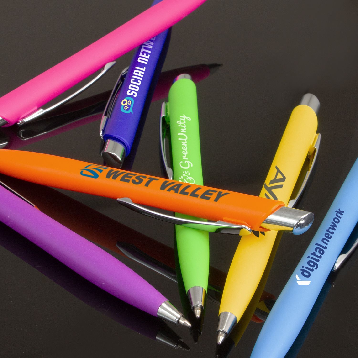 Assortment of colorful pens with company logos printed on them, including pink, purple, orange, green, yellow, and blue.