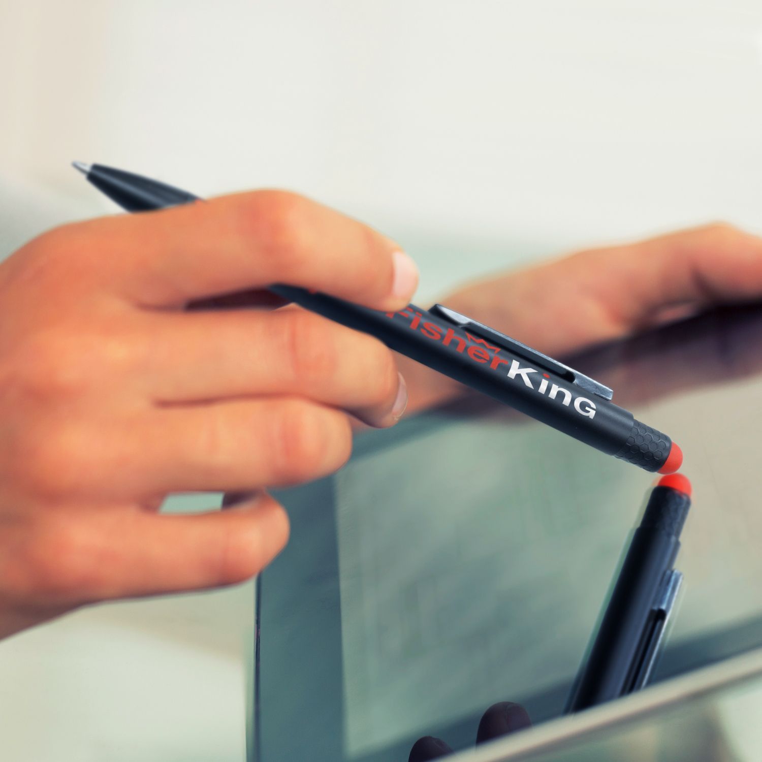 Person using a black pen with a red marker end, possibly a stylus, on a tablet. The pen has 