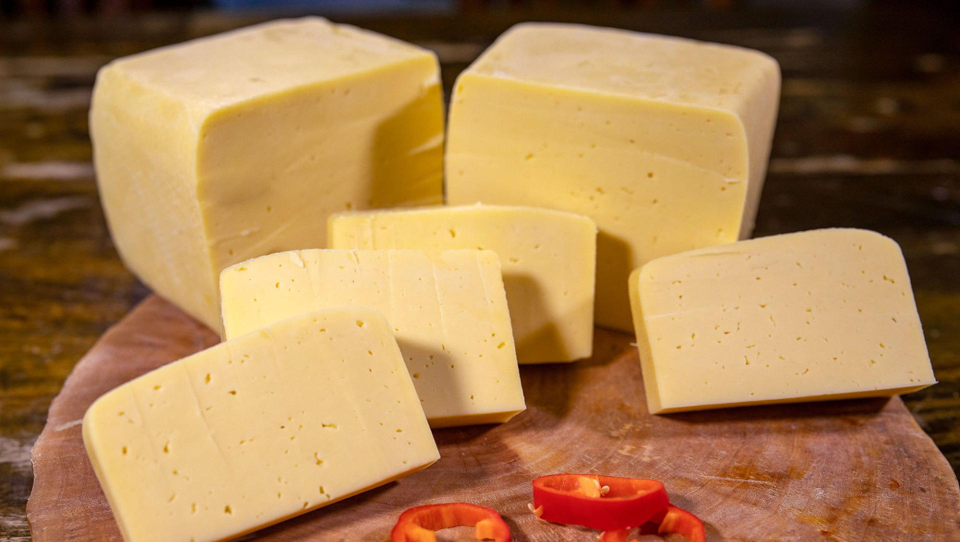 Ein hölzernes Schneidebrett mit mehreren Stücken Heidekäse und Paprika.