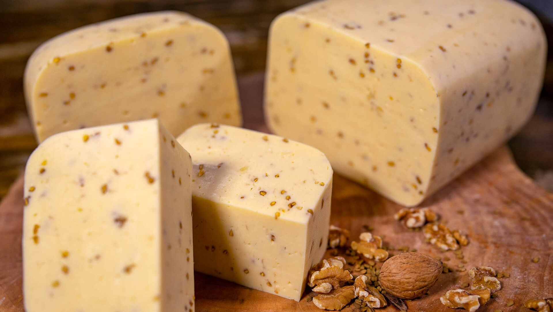 Ein hölzernes Schneidebrett mit vier verschieden großen Stücken Hofkäse mit Bockshornkleesamen. Davor Walnüsse.