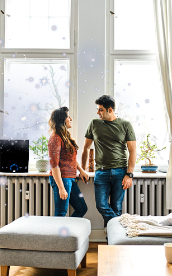 Two people chatting by a bright window in a modern living room with a couch and radiator