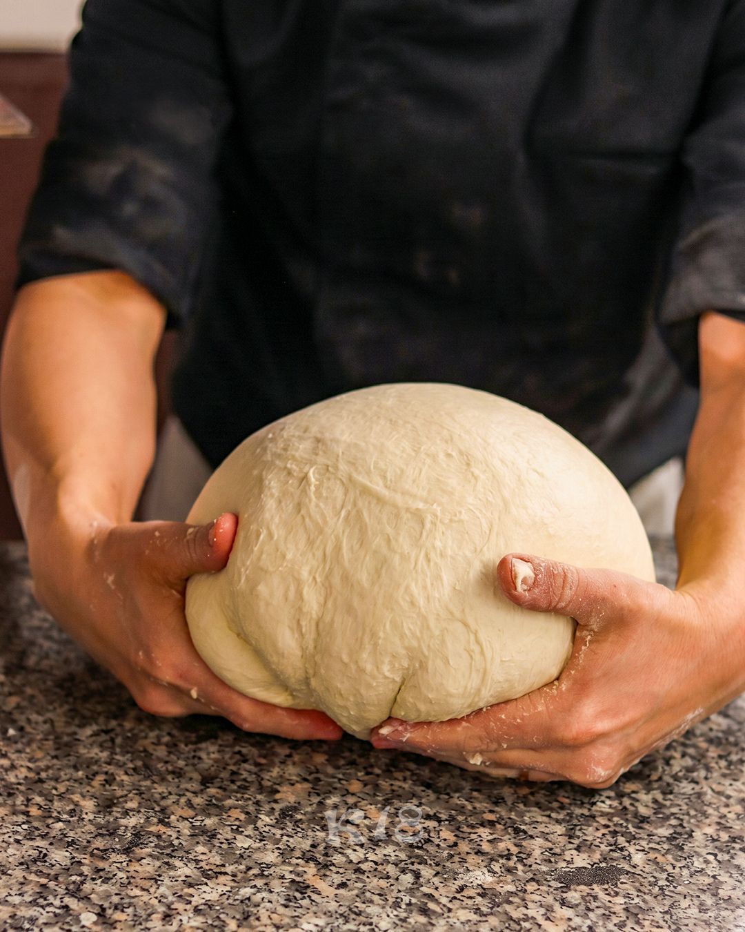 Mani che impastano una grossa palla di pasta su un piano di lavoro in granito