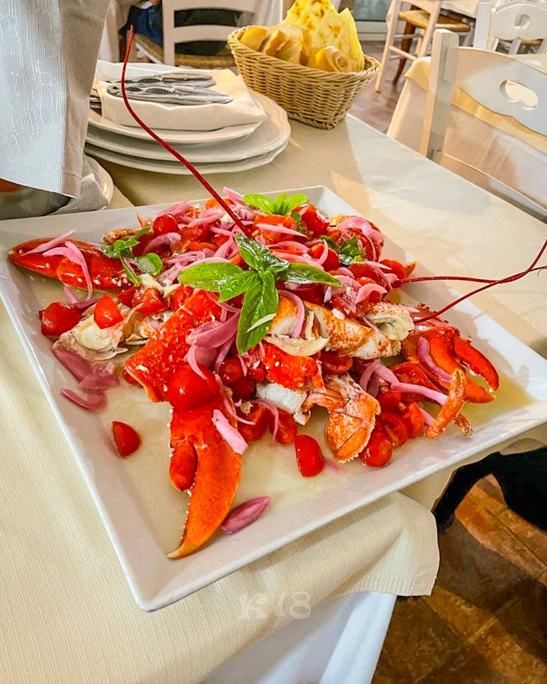 Insalata di aragosta e granchio su un piatto bianco, guarnita con verdure e pomodori, su un tavolo di ristorante.