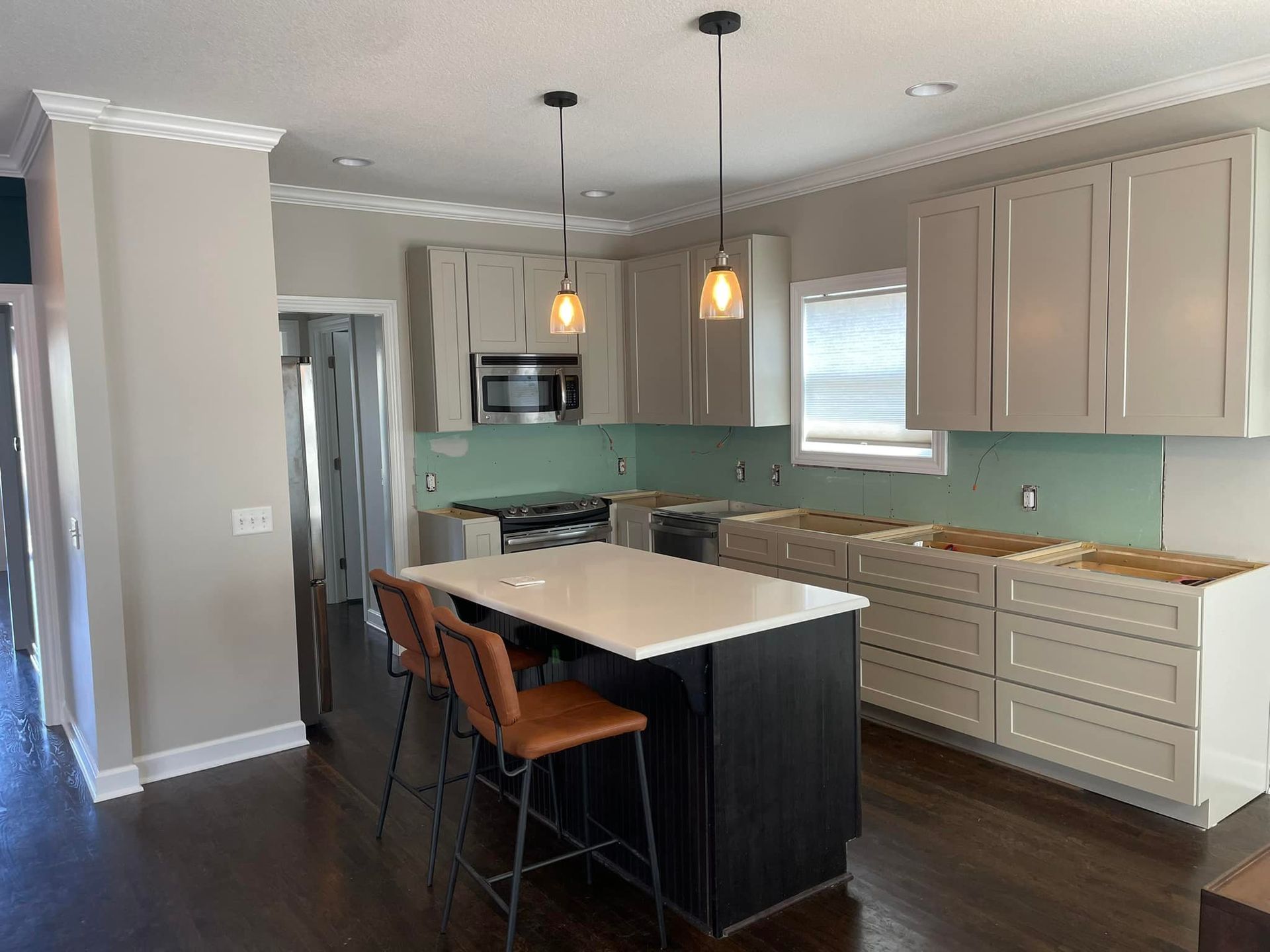 Kitchen with white cabinets, dark island, and brown bar stools, lit by hanging lights.