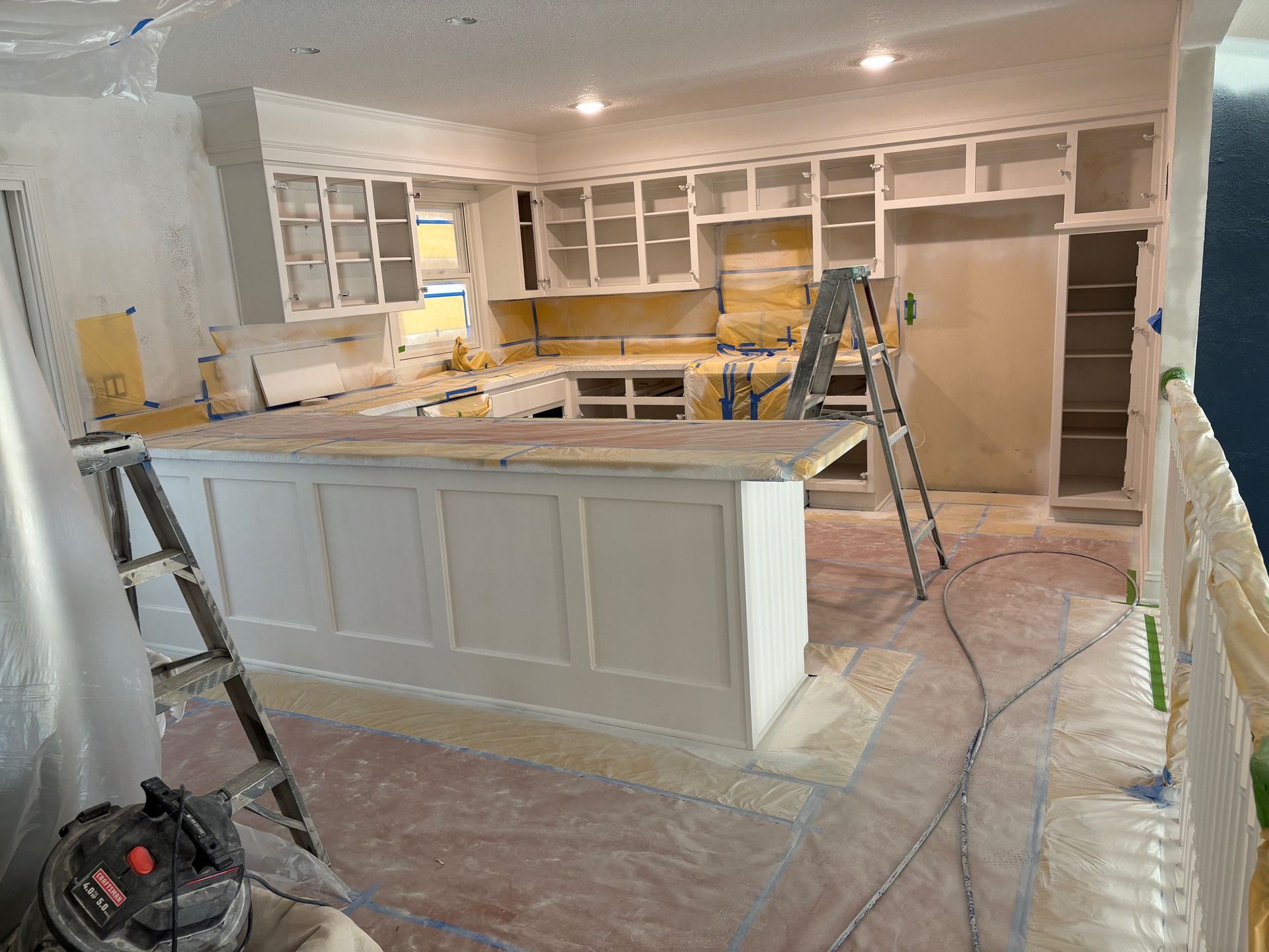 Kitchen renovation with white cabinets, island, and two step ladders on a dusty floor