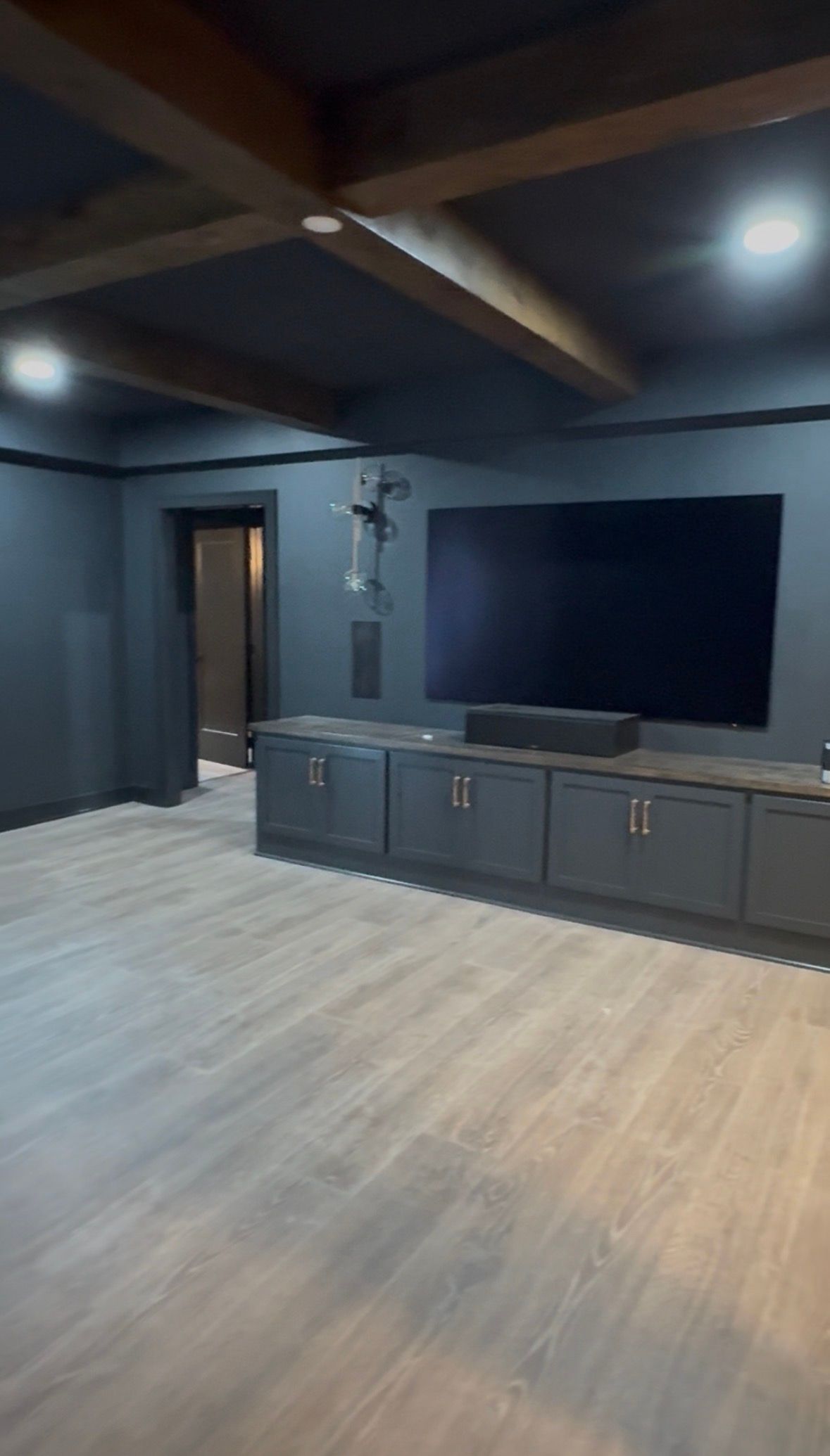 Modern living room with dark walls, wood floor, large TV, and gray media cabinet