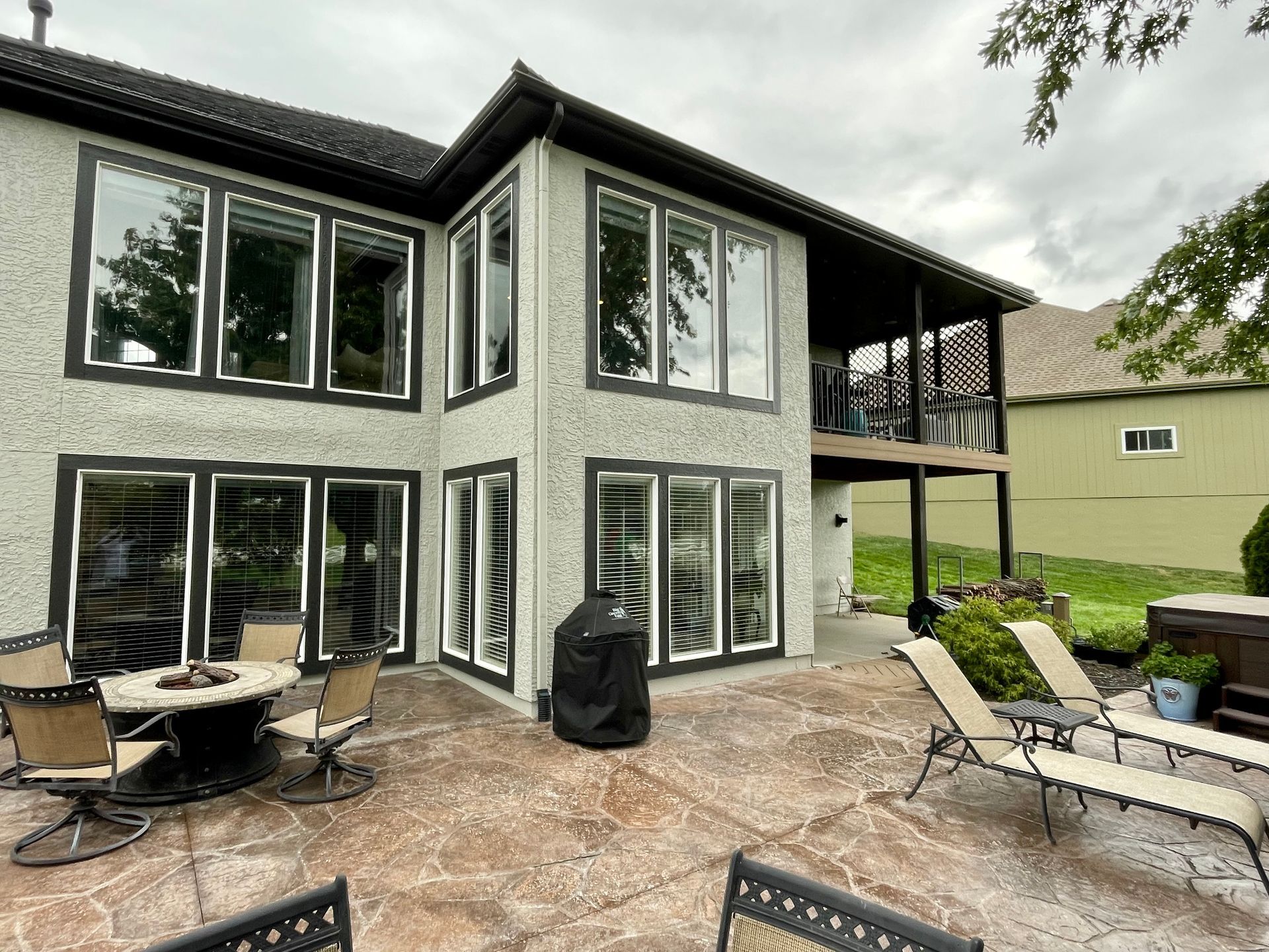 A light-colored house with a backyard patio featuring a stone-look floor, a round fire pit, and several lounge chairs.