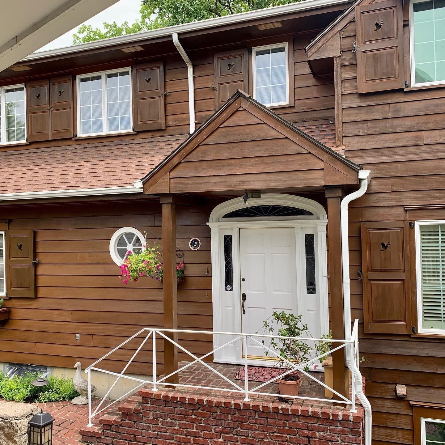 Brown, two-story house with white door, shutters, and railing. Brown siding and roof.