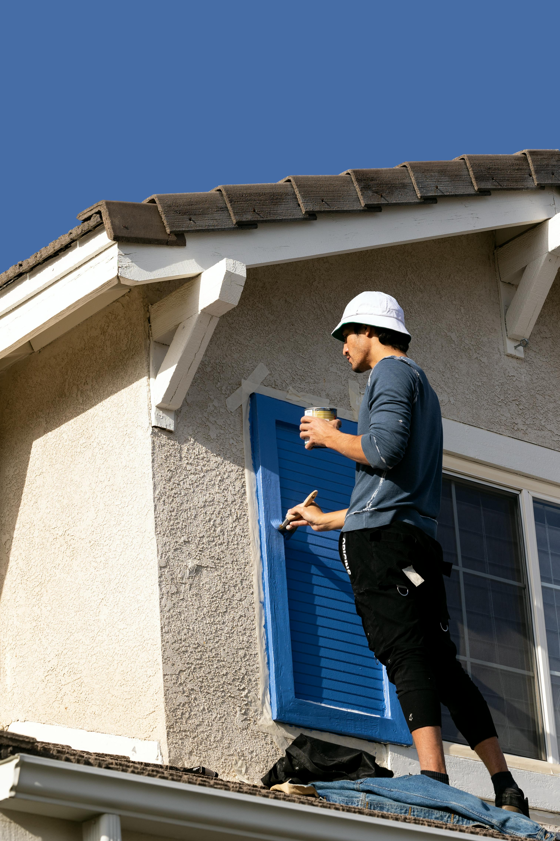 Worker in hard hat painting a house exterior on a ladder