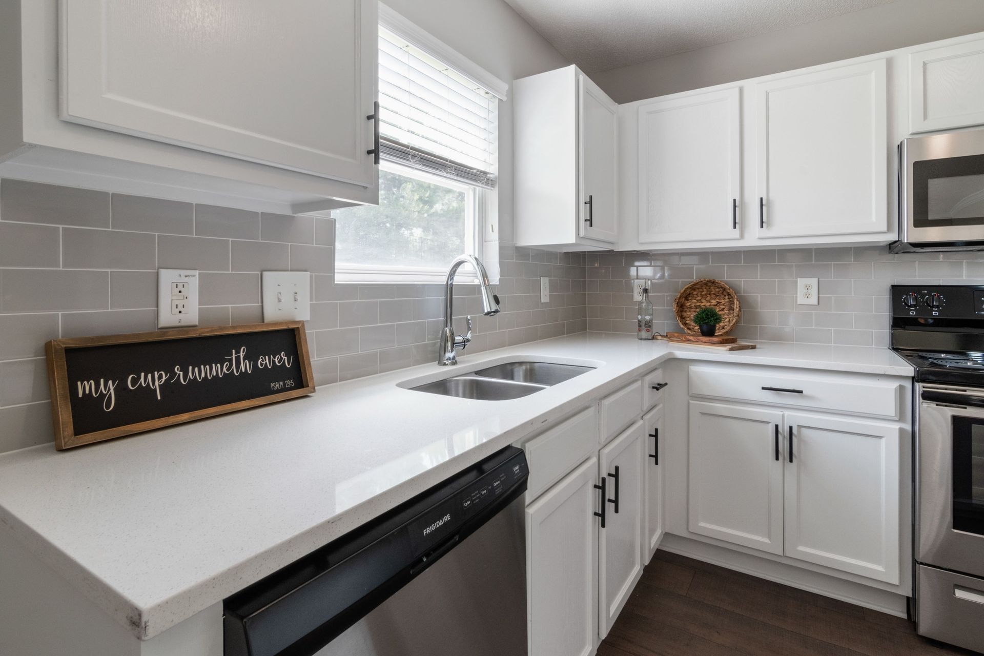 Bright white kitchen with gray tile backsplash, stainless appliances, and a small chalkboard sign by the sink