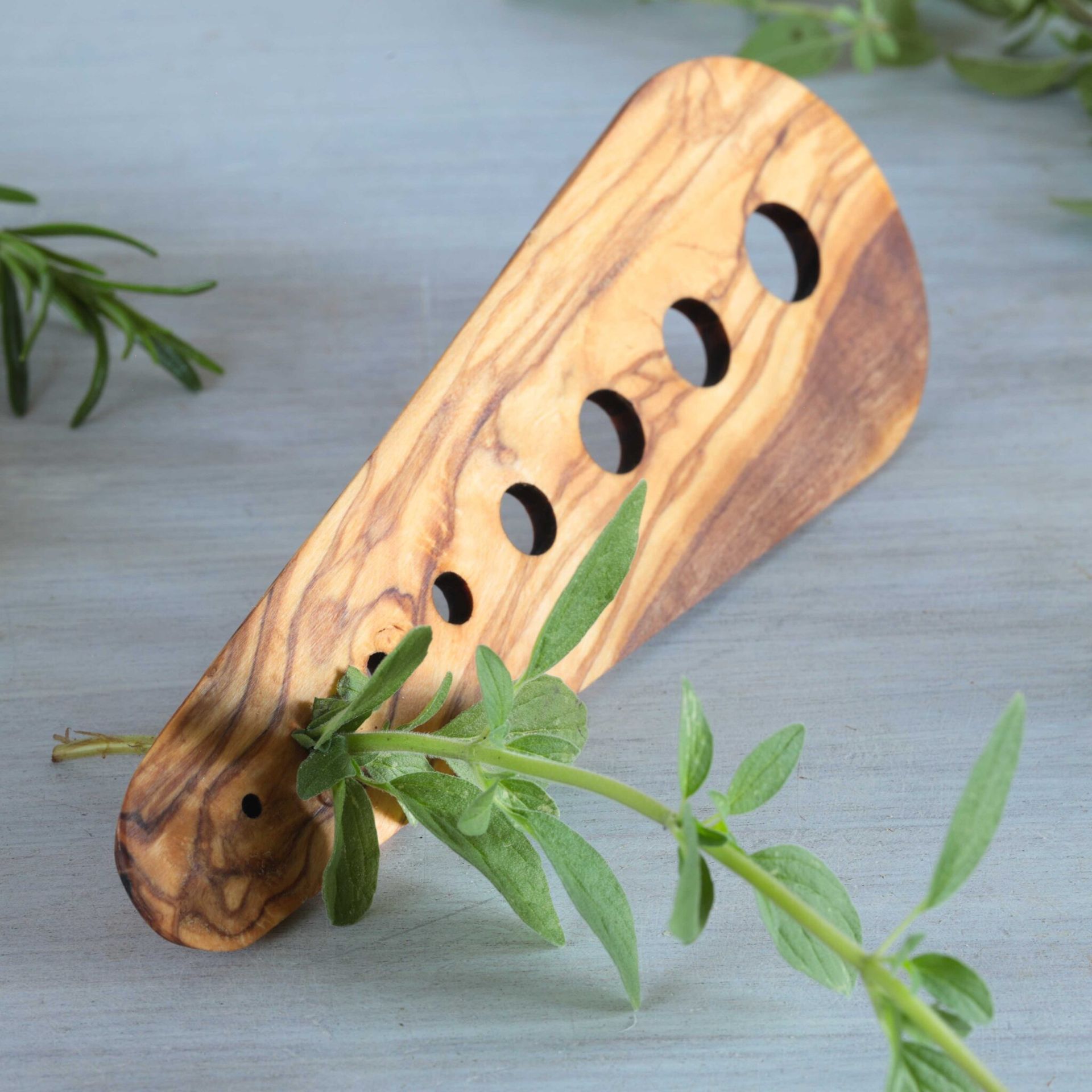 Olive wood herb stripper with holes, holding a sprig of green herbs.