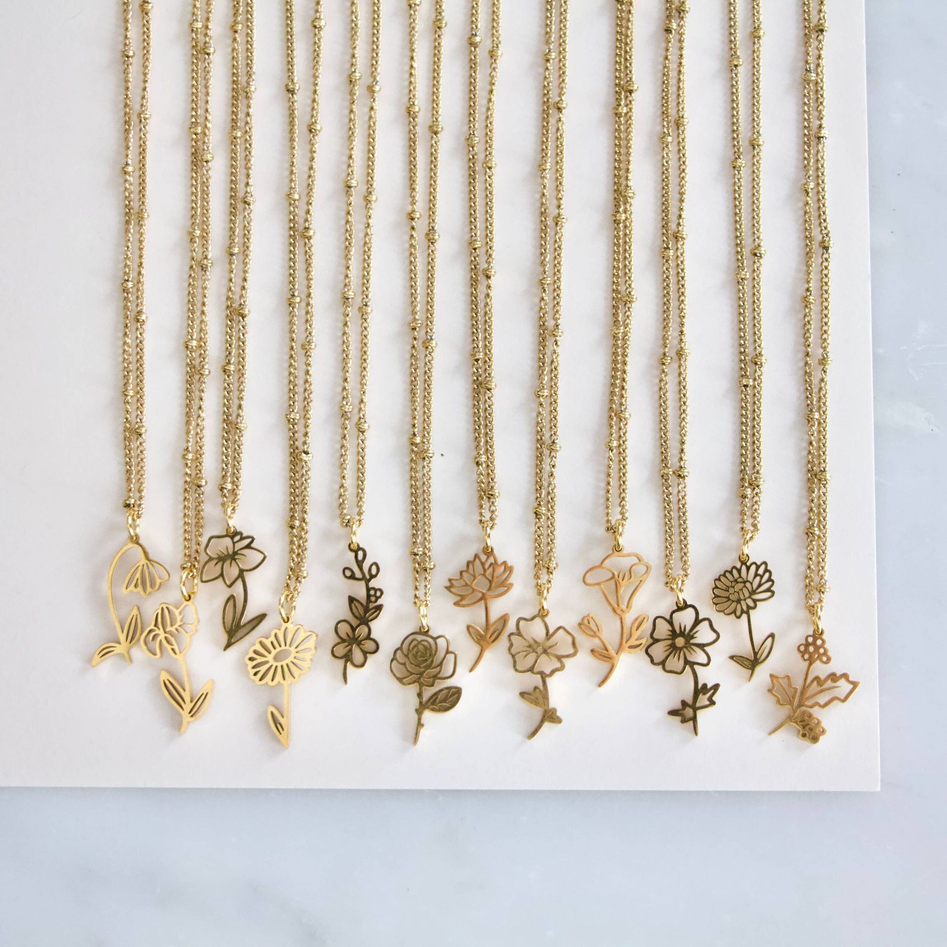 Gold flower pendant necklaces arranged on a white surface.