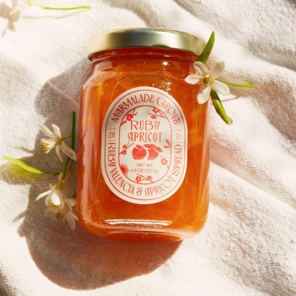 Jar of Ruby Apricot spread on a white cloth with small white flowers.