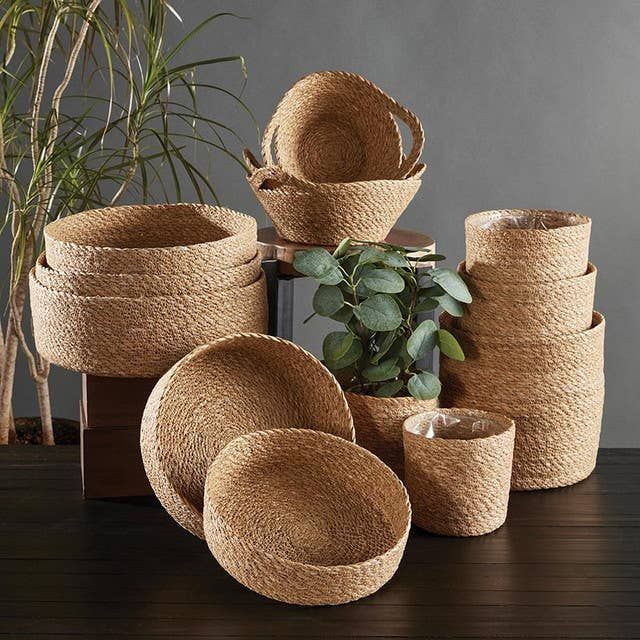 Assortment of woven natural fiber baskets of varying sizes. Some nest inside each other, with a plant in one.