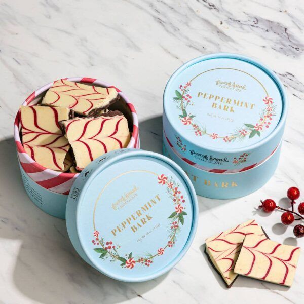 Peppermint bark in light blue round tins, with a red and white striped one opened, festive holiday treat.