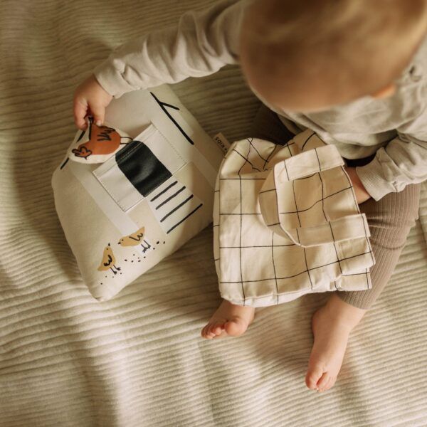 Baby playing with two fabric toy houses on a white bed.