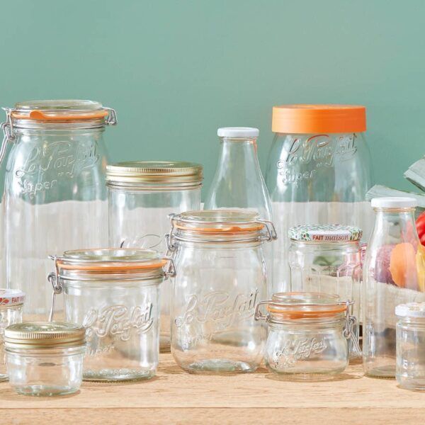 Glass jars with various closures arranged on a wooden surface against a teal backdrop.